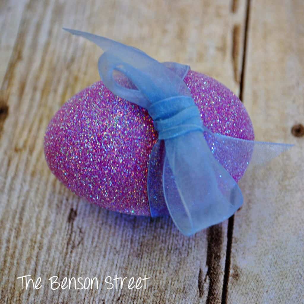 a purple egg with glitter on it with a bow tied around it