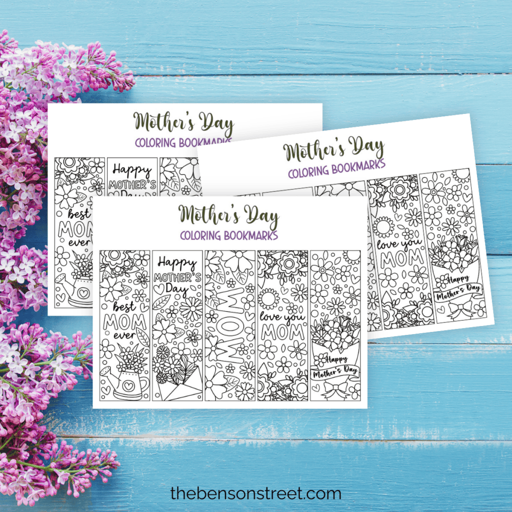 Printed out mother's day coloring bookmark sheets in a stack on a blue wood background with lilacs.