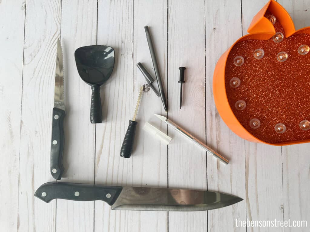 Tools for carving pumpkins laid out on a white washed wood background.