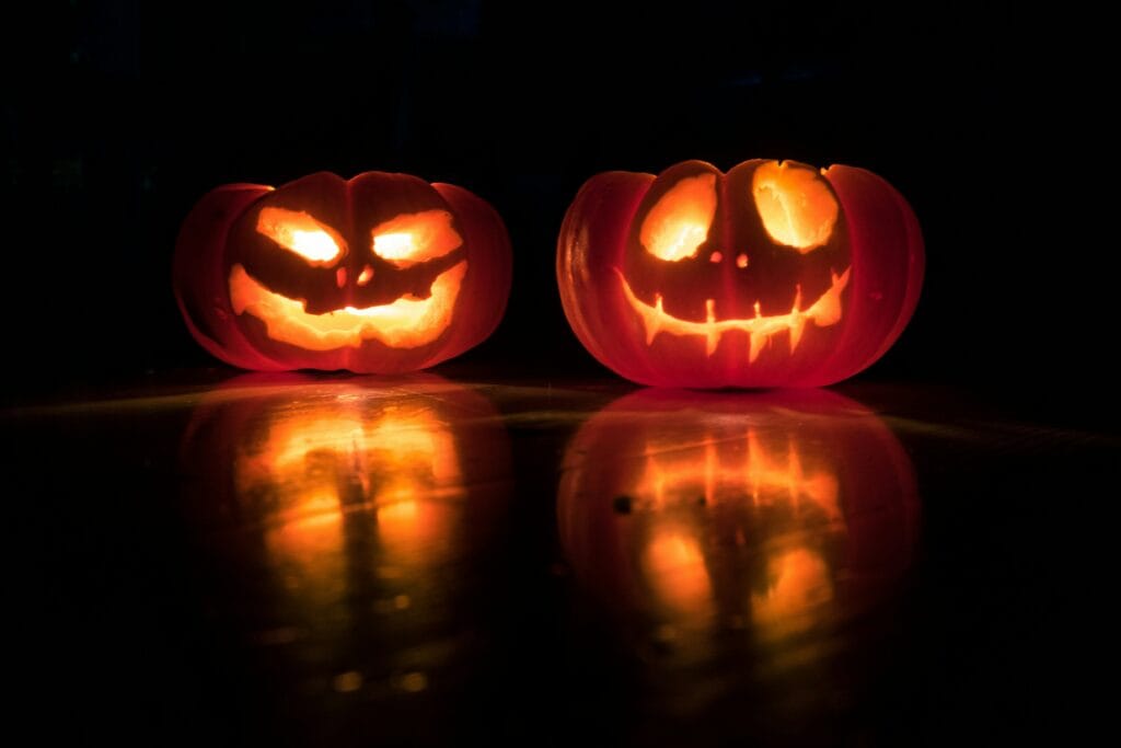 Two classic jack-o'lanterns lit up in the dark.