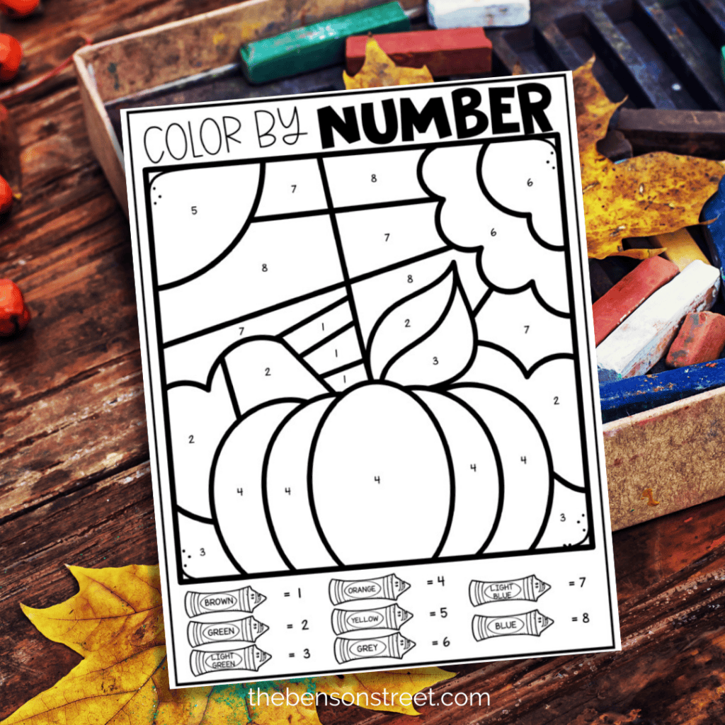 Pumpkin color by number page for fall with fall leaves and coloring supplies in background.
