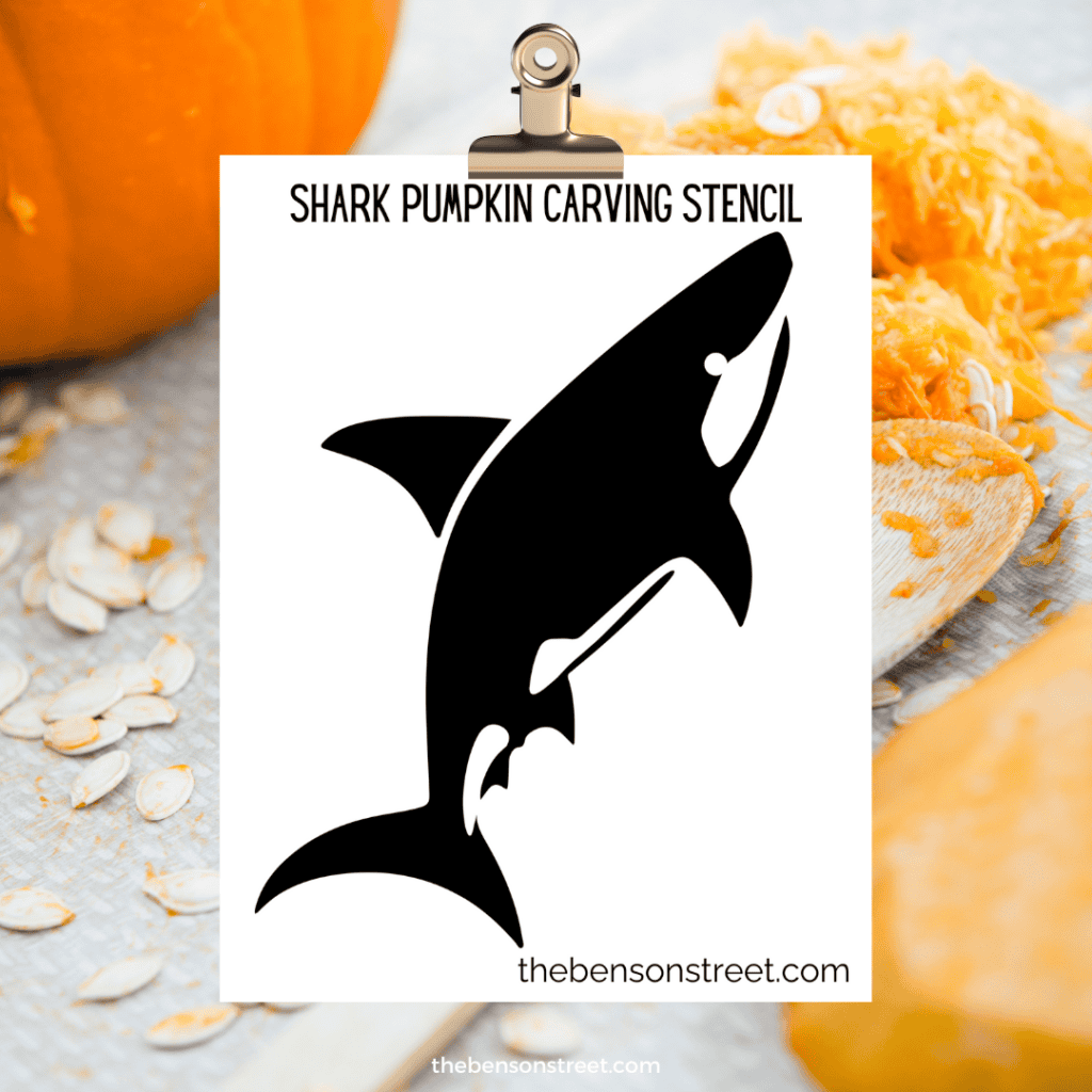 A printable shark pumpkin stencil, displayed on a wooden surface, with clear cut-out areas for easy transfer to a pumpkin.
