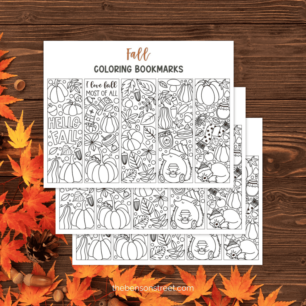 Three sheets of free printable fall coloring bookmarks laying on top of one another with a dark wood background and fall leaves.