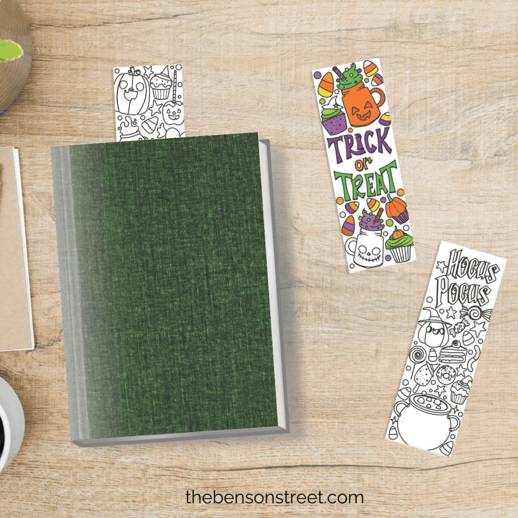Flat lay of a book with a bookmark in it and two coloring bookmarks for halloween on the table next to it.