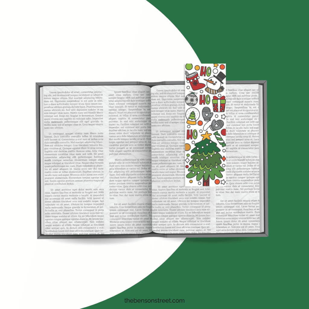 Open book laying flat with a colored in printable Christmas bookmark with a christmas tree and other holiday items.