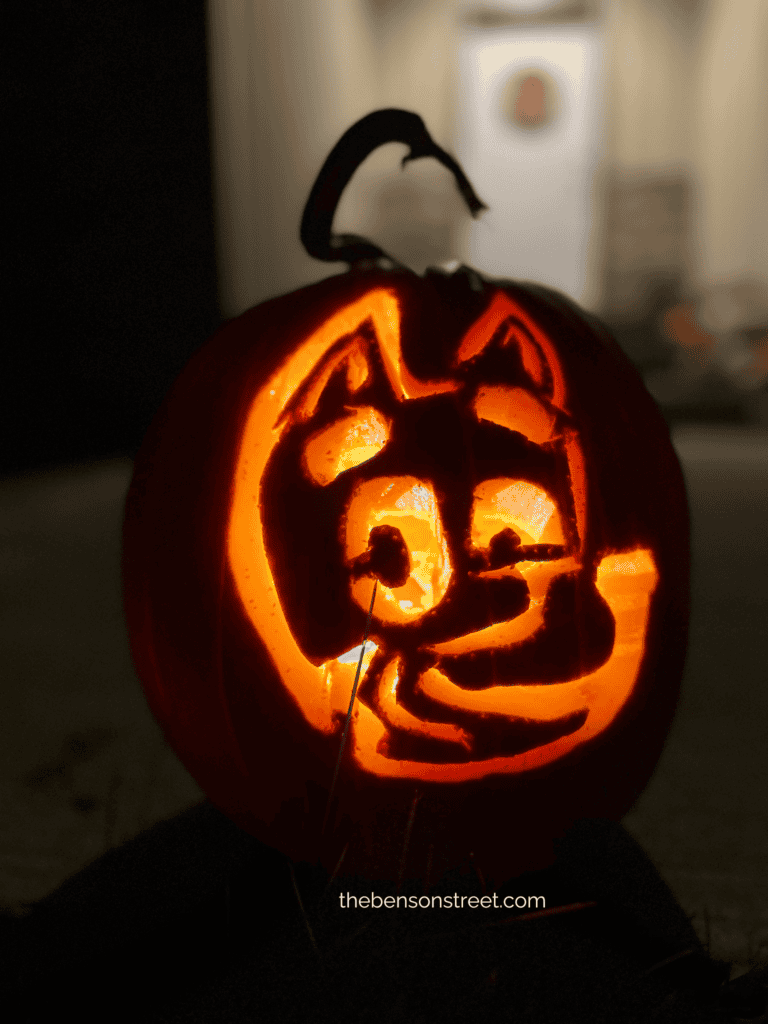 A pumpkin lit up with a carving of Bluey Heeler's Face.