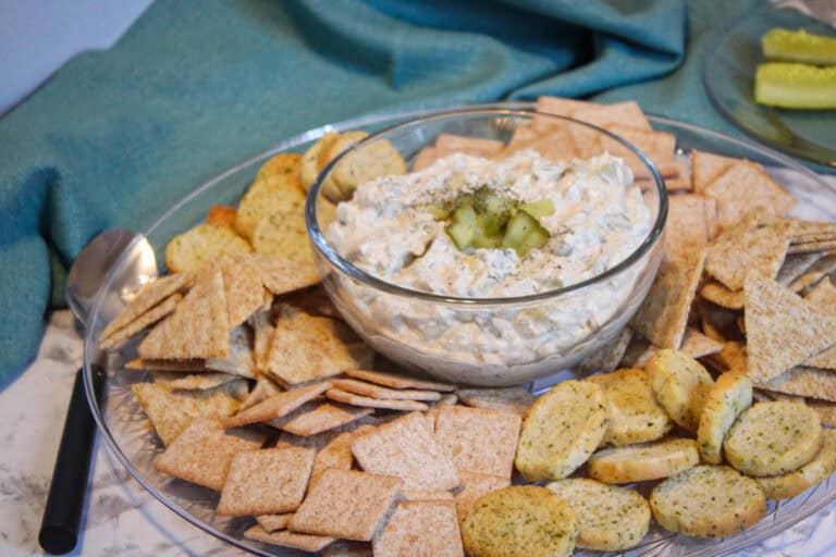 Close up shot of a bowl of dill pickle dip with crackers on a plate