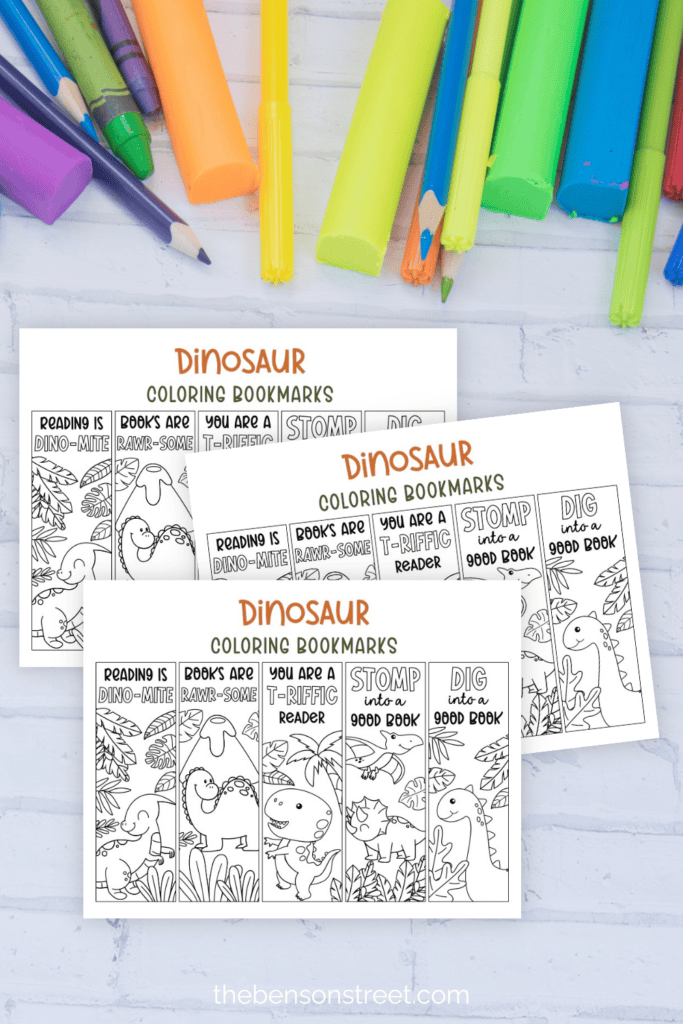 Coloring supplies surrounding three pages of coloring bookmarks with dinosaurs