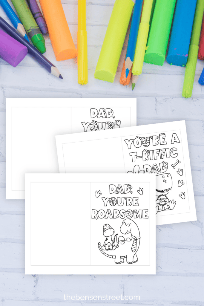 Three coloring cards for Father's Day with coloring supplies laying around them