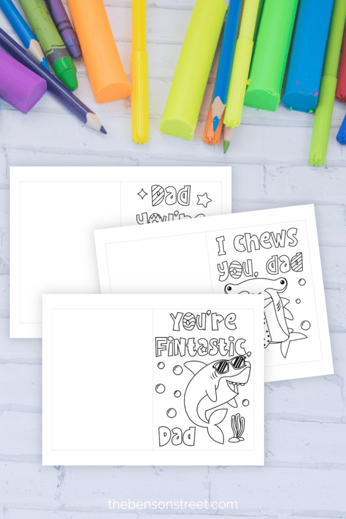 Three free printable Father's Day cards with coloring supplies in the background