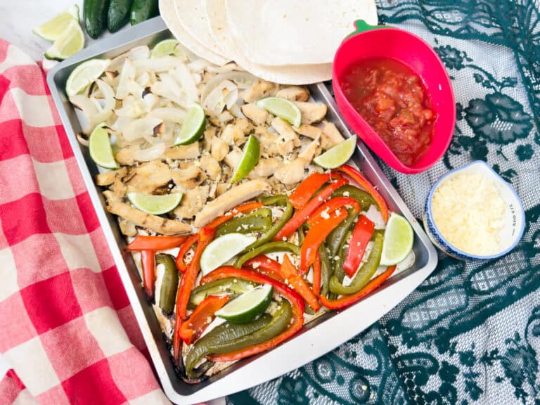 Chicken fajita filling straight from the oven, surrounded by small bowls of shredded cheese, avocado, and salsa.