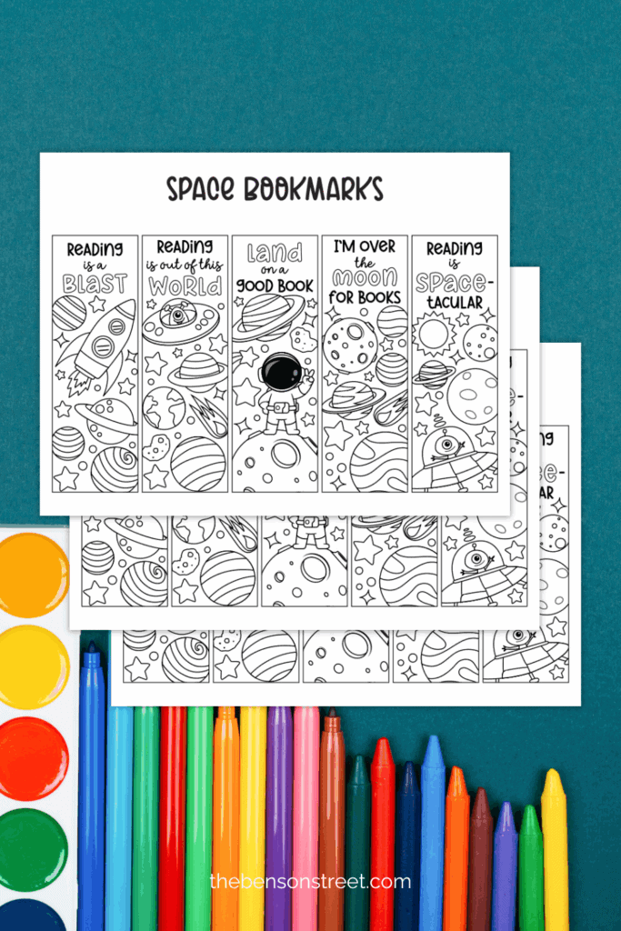 Three printed out black and white pages of space bookmarks on a background with coloring supplies