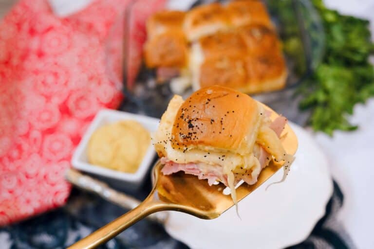 Up close shot of a baked ham and cheese slider being served on a spatula with poppy seeds on top