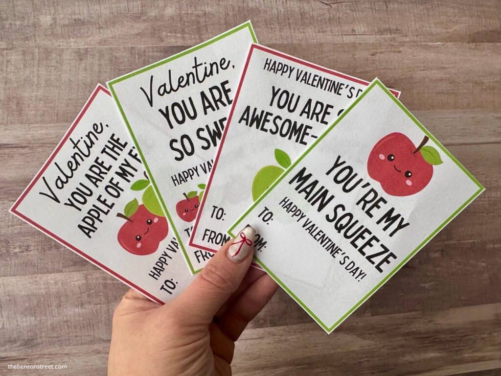 A hand holding four applesauce valentine cards