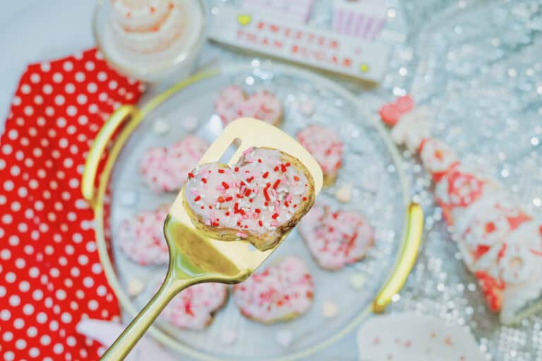 Up close shot of a heart cinnamon roll with strawberry frosting on a gold spatula