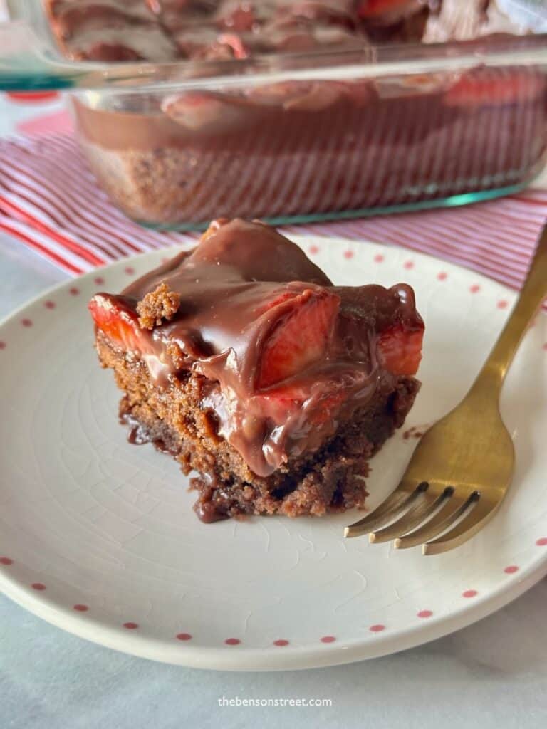 A pan of brownies next to a plate with a chocolate strawberry brownie on top