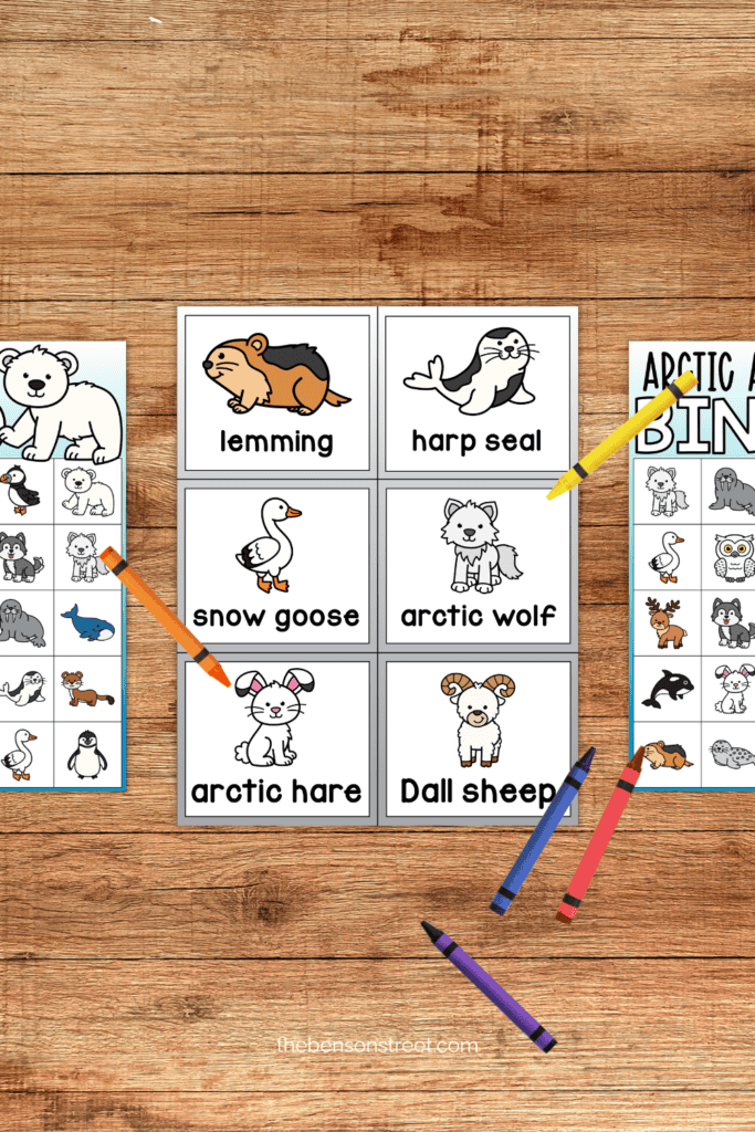 A table with calling cards and bingo boards with cold weather animals with crayons laying around