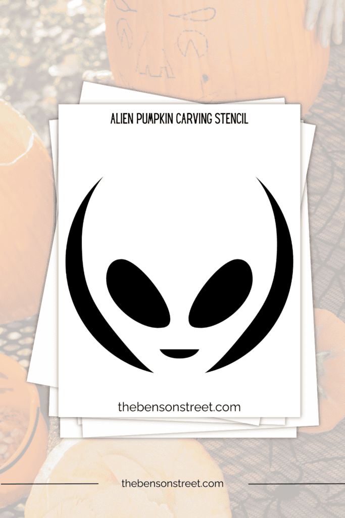 A stack of papers with a printable alien carving template for pumpkins on top