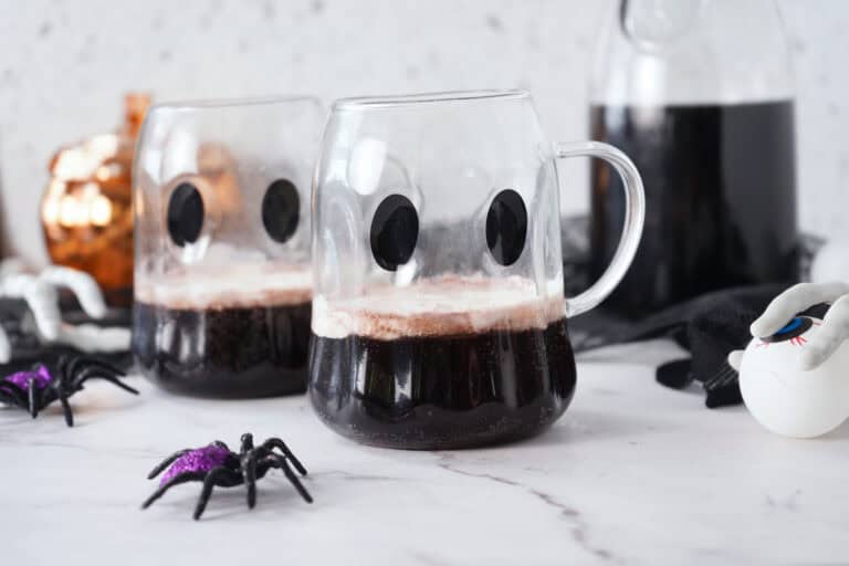 two mugs full of halloween punch for kids with halloween decorations